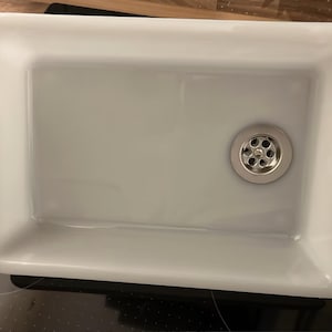 Könnte beinhalten: Rechteckiges Waschbecken aus weißer Keramik mit einem Abfluss aus Edelstahl. Das Waschbecken hat eine glatte, glänzende Oberfläche. Der Abfluss ist kreisförmig mit mehreren kleinen Löchern.