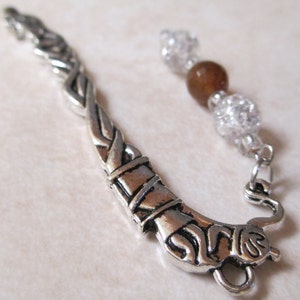 May include: Silver bookmark with a Celtic knot design and a brown and clear bead charm.