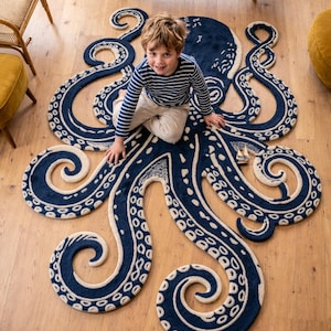 May include: A navy blue octopus rug with cream-coloured details, including the suckers on the tentacles. The rug is on a hardwood floor. A child is sitting on the rug. The rug is a decorative item for a child's room.