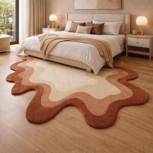 以下が含まれることがあります： 大きなベッドとニュートラルカラーの寝具、茶色とベージュの波型のラグがある寝室。 ラグのサイズは約200cm x 150cmです。 木の床の上に、2つのランプ付きのベッドサイドテーブルがベッドの両側にあります。