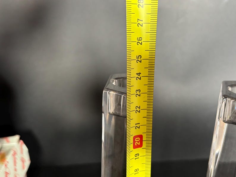 May include: A pair of silver-colored, hexagonal candle holders. A yellow ruler is placed next to one, showing a height of approximately 9 inches. The candle holders have a modern, geometric design.