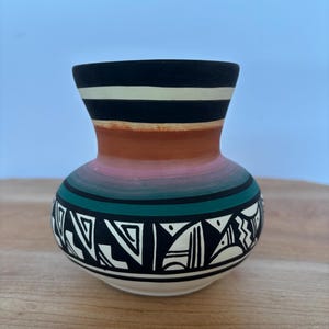 Peut inclure: Un vase en céramique peint à la main, avec une base large et un col étroit. Le vase présente un bord noir avec des rayures blanches et noires, une section médiane marron et une base avec des motifs géométriques noirs et blancs. Le vase mesure environ 15 cm de haut.