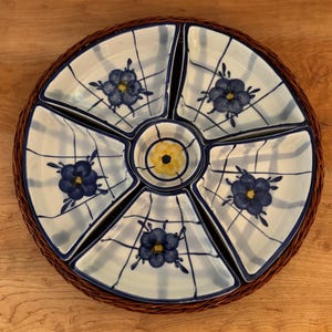 Könnte beinhalten: Ein geteilter Servierteller mit einem gewebten braunen Rand. Die weißen Keramikabschnitte sind mit blauen Blumenmustern und einem blauen Gittermuster verziert. Der Mittelteil ist gelb.