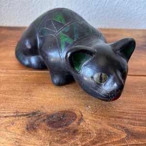Può includere: Una statuetta di gatto nero con motivi geometrici verdi sul dorso e sulle orecchie. Il gatto ha occhi a mandorla con pupille verticali, una finitura opaca liscia e una postura accovacciata. La scultura è realizzata con toni scuri.