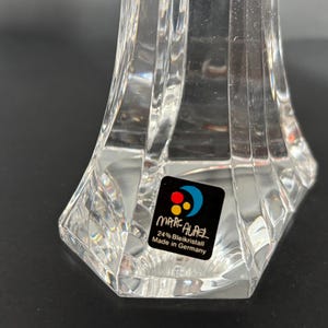 May include: Clear crystal decorative object with a faceted design. The base is hexagonal, and the object has a flared shape. A sticker on the base reads "MARC AUREL 24% Bleikristall Made in Germany."