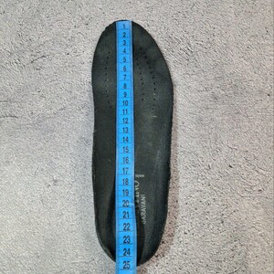 May include: A black shoe insole with a blue measuring tape alongside it. The insole is approximately 11 inches long. The insole has small perforations and the text "GARAVANI" is visible. The background is a textured gray surface.
