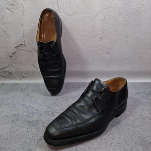 Op de afbeelding: Twee zwarte leren herenschoenen met veters. De schoenen hebben een vierkante neus en staan tegen een grijze achtergrond. De schoenen zijn een klassieke stijl, geschikt voor formele gelegenheden.