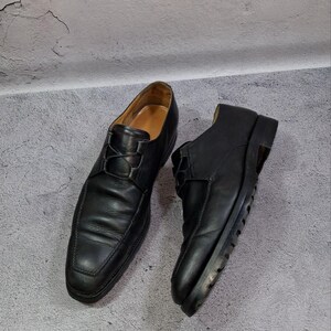 Op de afbeelding: Een paar zwarte leren herenschoenen. De schoenen hebben een klassiek ontwerp met een vetersluiting en een vierkante neus. De zolen zijn zwart en de binnenkant is lichtbruin.