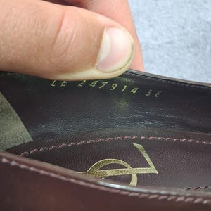 May include: Close-up of a burgundy leather shoe interior. The shoe features a gold logo and the numbers "LE 247914 36" are visible. The interior is stitched with a contrasting pink thread.