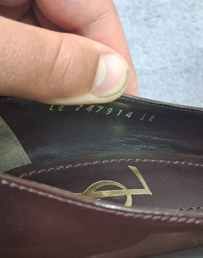 May include: Close-up of a burgundy leather shoe interior. The shoe features a gold logo and the numbers "LE 247914 36" are visible. The interior is stitched with a contrasting pink thread.