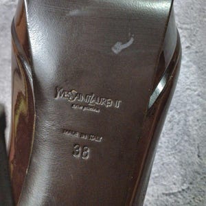 May include: Close-up of the sole of a brown high-heeled shoe. The brand name "Yves Saint Laurent" is embossed on the sole, along with "MADE IN ITALY" and the size "38".