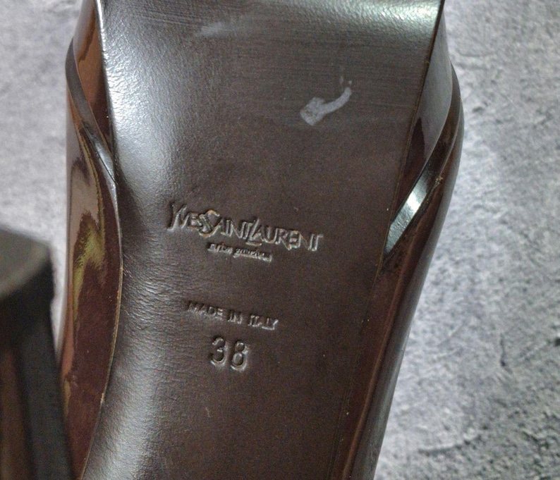 May include: Close-up of the sole of a brown high-heeled shoe. The brand name "Yves Saint Laurent" is embossed on the sole, along with "MADE IN ITALY" and the size "38".