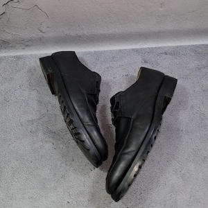 Op de afbeelding: Een paar zwarte leren schoenen met een laag uitgesneden ontwerp. De schoenen hebben een vetersluiting en een dikke zool. De schoenen worden gepresenteerd tegen een grijze achtergrond.