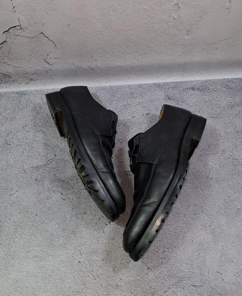 Op de afbeelding: Een paar zwarte leren schoenen met een laag uitgesneden ontwerp. De schoenen hebben een vetersluiting en een dikke zool. De schoenen worden gepresenteerd tegen een grijze achtergrond.