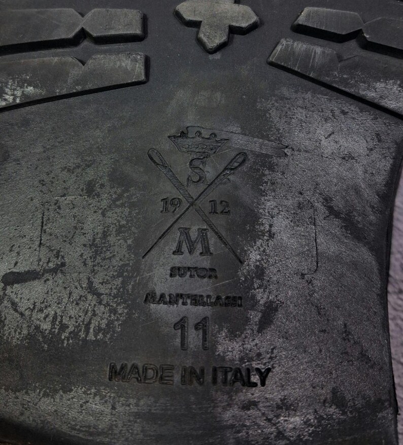 Op de afbeelding: Een witte keramische mok met een zwart handvat en de tekst "But First, Coffee" in een zwarte, handgeschreven lettertype. De mok staat op een wit oppervlak.