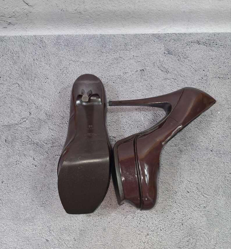 May include: A pair of brown platform high heels. The shoes have a glossy finish, a square toe, and a thin stiletto heel. The platform sole adds height and a modern touch to the classic design.