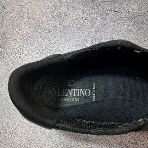 May include: Close-up of a black shoe interior. The shoe features the brand name "VALENTINO GARAVANI" in white lettering. The words "MADE IN ITALY" are also visible. The shoe appears to be made of a mesh material.