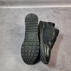 May include: Black sneakers with a textured sole and a combination of suede and leather panels. The sole is thick and features a grid-like pattern. The sneakers are displayed against a gray background.