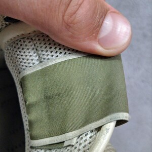 K&ouml;nnte beinhalten: Ein Schuhbestandteil mit einer Basis aus hellbeigem Netzstoff und einem glatten, olivgr&uuml;nen Stoffriemen. Das Design umfasst einen geschwungenen, hellbeigen Rand, der den olivgr&uuml;nen Bereich einfasst und f&uuml;r eine geschichtete, strukturierte Optik sorgt.