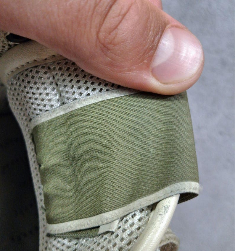 K&ouml;nnte beinhalten: Ein Schuhbestandteil mit einer Basis aus hellbeigem Netzstoff und einem glatten, olivgr&uuml;nen Stoffriemen. Das Design umfasst einen geschwungenen, hellbeigen Rand, der den olivgr&uuml;nen Bereich einfasst und f&uuml;r eine geschichtete, strukturierte Optik sorgt.