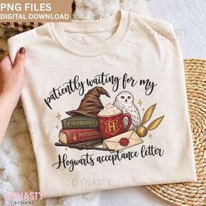 Puede incluir: Una camiseta de color crema con un estampado gráfico que incluye el texto "patiently waiting for my Hogwarts acceptance letter". El diseño muestra un sombrero de mago marrón, dos libros etiquetados como "Herbology" y "Potions", una taza roja, un búho y una carta.