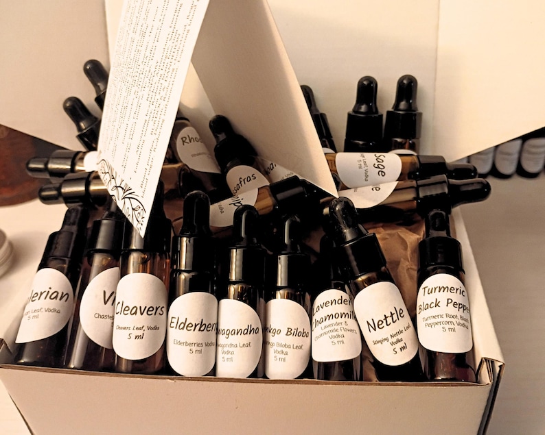 May include: A box filled with small brown glass bottles with black droppers. Each bottle has a white label with text, including "Valerian," "Cleavers," and "Nettle." The box also contains a folded paper with text.
