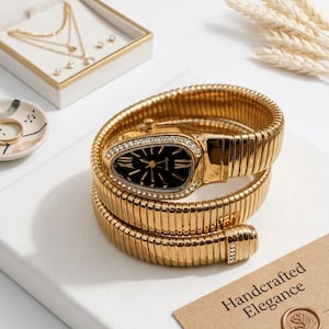 May include: A gold-coloured wristwatch with a black face and diamond detailing, coiled around itself. The watch is displayed with a jewellery box containing necklaces and earrings, and a card that reads "Handcrafted Elegance."