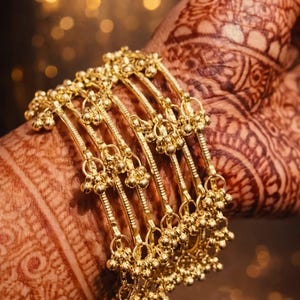 May include: Gold bangles with detailed beadwork, displayed on a hand decorated with henna patterns. The bangles are a traditional design, with small dangling beads, creating a rich, cultural aesthetic.