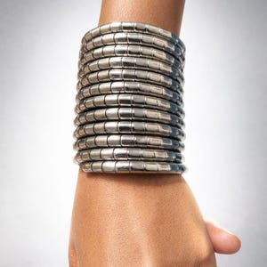 May include: A silver-toned bracelet composed of numerous cylindrical segments, stacked to create a wide, cuff-like design. The bracelet is worn on a wrist, showcasing its metallic sheen. The date "21 April 2024" is visible.