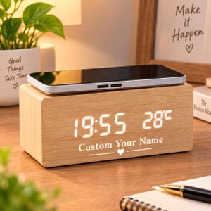 May include: A rectangular light wood digital alarm clock with a wireless charging top surface. The front display shows the time 19:55 and temperature 28°C in white LED digits. The text Custom Your Name is printed below the display with a heart icon.