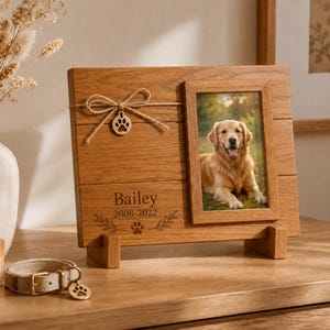 Puede incluir: Un marco conmemorativo de madera para mascotas con diseño de tablones horizontales, un lazo de cuerda con un dije de huella y el nombre Bailey grabado junto a los años 2008-2022. El marco contiene una fotografía vertical de un perro golden retriever.
