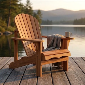 May include: A natural wood Adirondack chair with a curved backrest, wide armrests, and a low-slung seat. A grey fabric throw blanket is draped over the seat, and a plain ceramic mug sits on the flat surface of the right armrest.