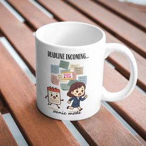 Könnte beinhalten: Ein weißer Keramikbecher mit dem Text "DEADLINE INCOMING..." oben und "panic mode" unten. Die Grafik zeigt eine Zeichentrickfigur, die neben einem Kalender-Charakter rennt, umgeben von Haftnotizen mit der Aufschrift "2 DAYS TO GO".