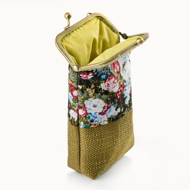 May include: A small, floral patterned pouch with a gold metal clasp. The pouch is made of a brown fabric with a floral pattern and a green fabric lining. The pouch is open and the lining is visible.