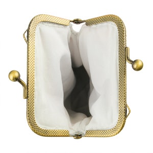 May include: An open, antique-style coin purse with a rectangular frame and a brass finish. The interior is lined with white fabric. The purse has a clasp closure and a decorative, textured border.