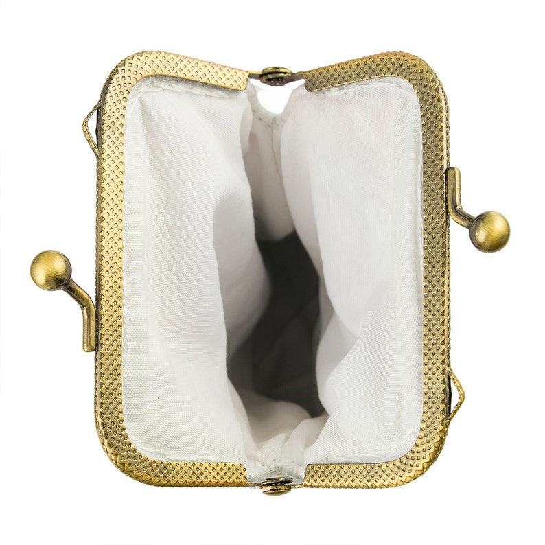 May include: An open, antique-style coin purse with a rectangular frame and a brass finish. The interior is lined with white fabric. The purse has a clasp closure and a decorative, textured border.
