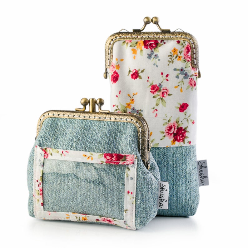 May include: Two vintage-style coin purses with kiss-lock closures. One is a small, square purse with a clear window and a floral border. The other is a tall, rectangular glasses case. Both have a blue-green textured fabric base and a floral pattern.