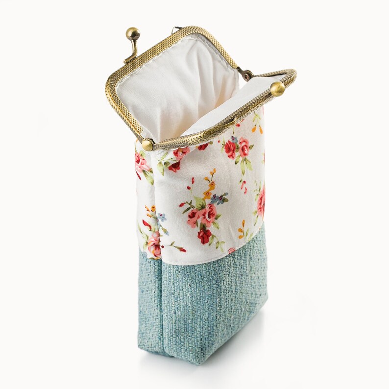 May include: An open, rectangular coin purse with a metal clasp. The top half features a white fabric with a floral pattern in pink, red, and yellow. The bottom half is a textured, light blue fabric.
