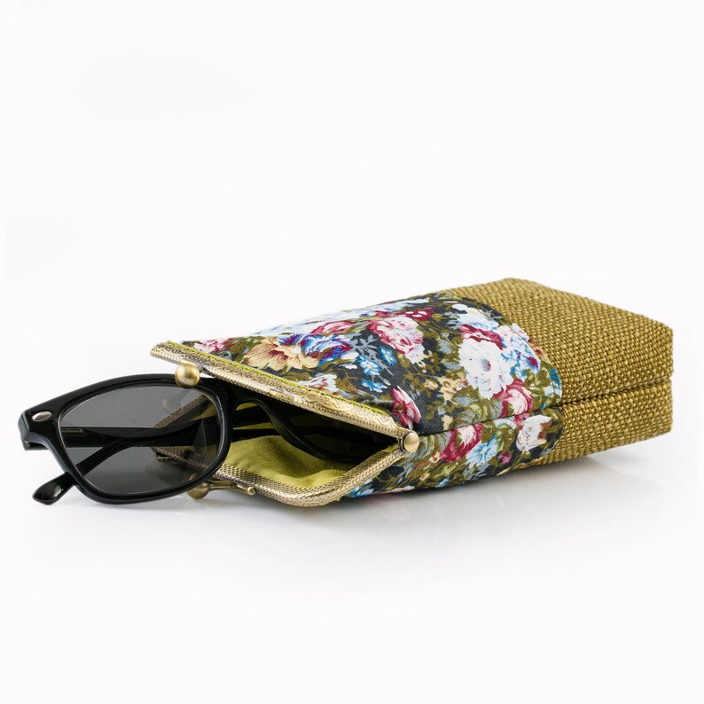 May include: A floral patterned glasses case with a gold zipper and a brown burlap flap. The case is open and a pair of black sunglasses are partially inside.