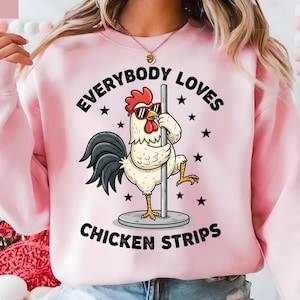 May include: Pink sweatshirt with the text "EVERYBODY LOVES CHICKEN STRIPS." The graphic features a cartoon rooster wearing sunglasses and posing on a pole. Black stars are scattered around the text and image.