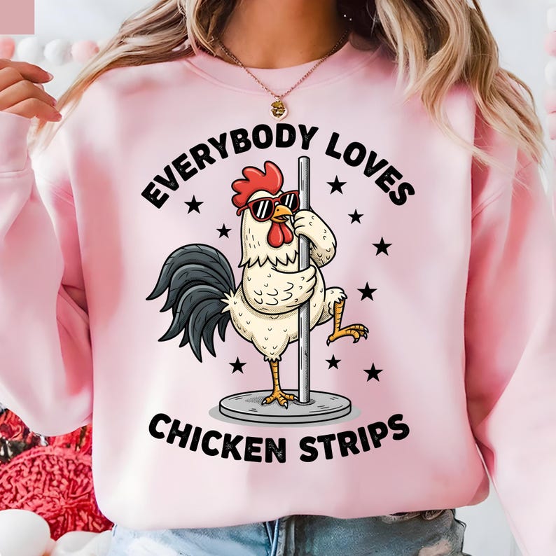 May include: Pink sweatshirt with the text "EVERYBODY LOVES CHICKEN STRIPS." The graphic features a cartoon rooster wearing sunglasses and posing on a pole. Black stars are scattered around the text and image.
