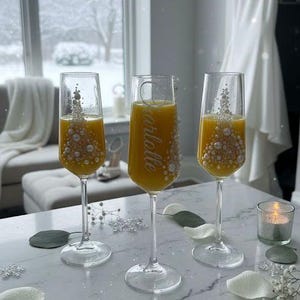 Puede incluir: Tres copas de champ&aacute;n de cristal transparente llenas de zumo de naranja. Dos copas presentan un dise&ntilde;o decorativo de &aacute;rbol hecho de perlas blancas. La copa central est&aacute; grabada con el nombre Charlotte en letra cursiva, con perlas en el lateral.