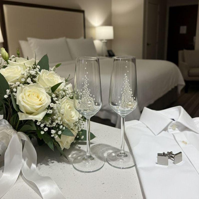 Puede incluir: Un ramo de rosas blancas y paniculata con una cinta blanca, dos copas de champ&aacute;n de cristal transparente decoradas con peque&ntilde;as perlas blancas, una camisa blanca de botones y un par de gemelos de metal plateado.