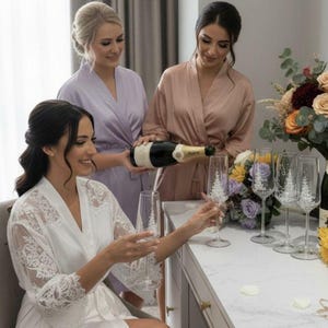 Puede incluir: Un juego de copas de champ&aacute;n de cristal transparente con un delicado dise&ntilde;o de pino grabado en blanco en el c&aacute;liz. Las copas tienen un tallo fino y una base circular, expuestas junto a una botella de vino espumoso y arreglos florales.