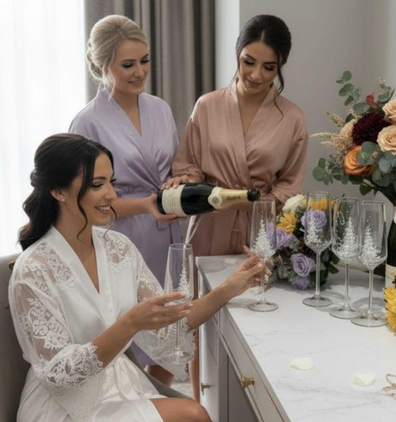 Puede incluir: Un juego de copas de champ&aacute;n de cristal transparente con un delicado dise&ntilde;o de pino grabado en blanco en el c&aacute;liz. Las copas tienen un tallo fino y una base circular, expuestas junto a una botella de vino espumoso y arreglos florales.