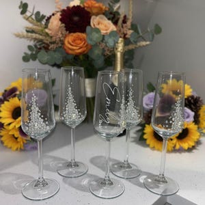 Puede incluir: Cinco copas de champ&aacute;n de cristal transparente con tallos delgados y bases circulares. Cuatro copas presentan un dise&ntilde;o triangular decorativo de peque&ntilde;as perlas blancas y cristales. Una copa central est&aacute; personalizada con el texto Emily Bride en blanco.