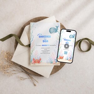 May include: A rectangular invitation card and a smartphone displaying the same design, featuring watercolor illustrations of a blue whale, a red crab, and sea plants. The text reads Join Us Oneder The Sea to celebrate Noah's first birthday.