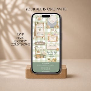 May include: A smartphone displaying a digital baby shower invitation on a green and white gingham background. The screen features illustrations of a wooden sign, a basket, and a market stall, with text including RSVP, Maps, Registry, and a countdown timer.