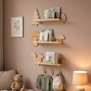 May include: Wooden shelves in the shape of a tree, mushroom, and squirrel are mounted on a pink wall. The shelves hold children's books. A green cardigan, a backpack, and a stuffed bear are also in the image.