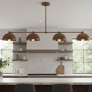 May include: A kitchen interior with a bronze four-light pendant lamp. The lampshades are dome-shaped. The kitchen has a white countertop, dark cabinets, and a white brick backsplash. Windows provide natural light.